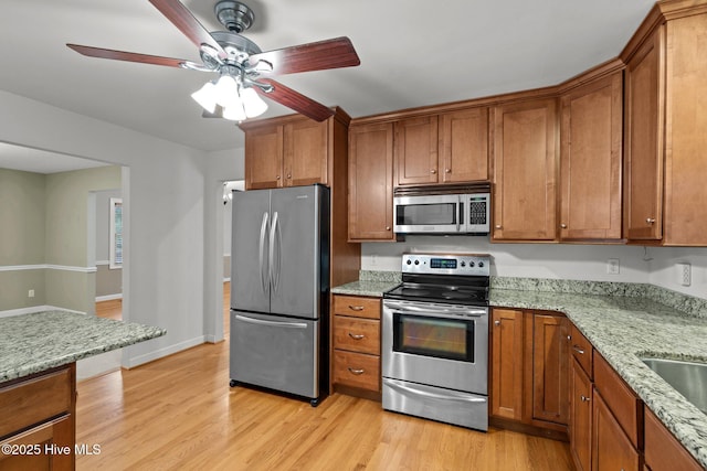 kitchen featuring light stone countertops, light wood finished floors, appliances with stainless steel finishes, and brown cabinets