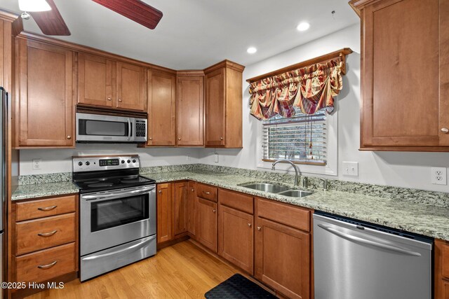 kitchen featuring stainless steel appliances, light wood finished floors, a sink, and brown cabinets