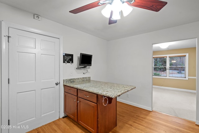 kitchen featuring brown cabinets, a ceiling fan, light stone countertops, light wood-type flooring, and baseboards