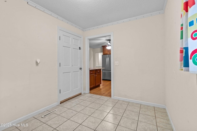 empty room with a textured ceiling, light tile patterned floors, visible vents, baseboards, and crown molding