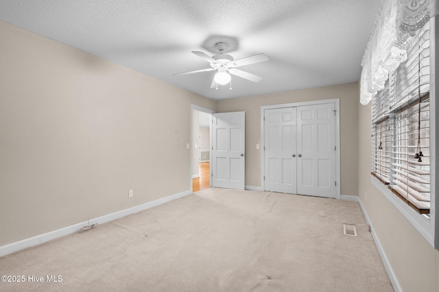 unfurnished bedroom featuring light carpet, baseboards, visible vents, a textured ceiling, and a closet