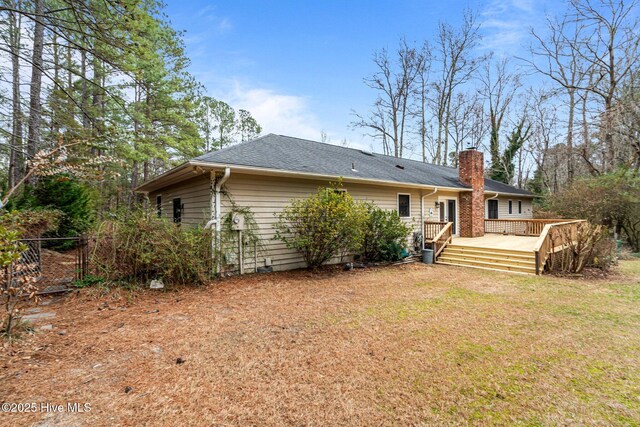 rear view of property with a deck, fence, roof with shingles, a lawn, and a chimney