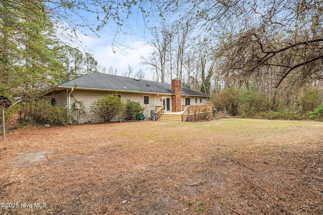 rear view of property featuring a chimney and a yard