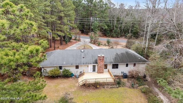 exterior space featuring a wooded view, a wooden deck, a chimney, a yard, and central AC unit