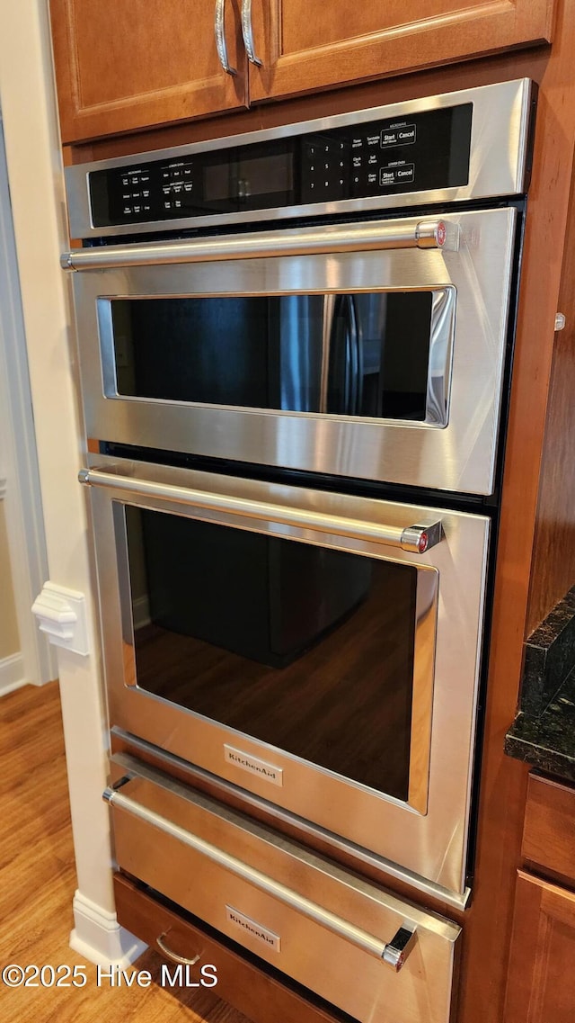 interior details featuring brown cabinetry, stainless steel double oven, dark stone counters, and light wood-style floors