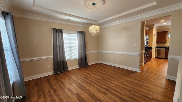 spare room with a tray ceiling, dark wood-style flooring, an inviting chandelier, ornamental molding, and baseboards