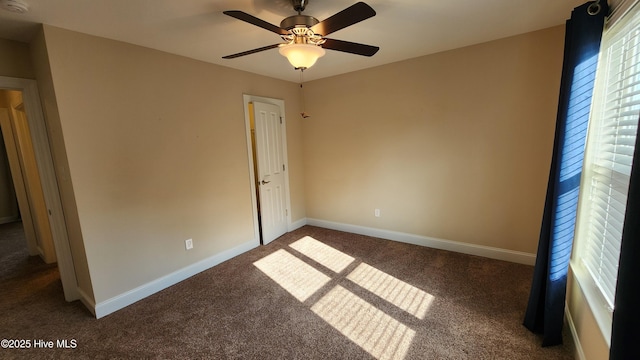 unfurnished room with a ceiling fan, dark colored carpet, and baseboards