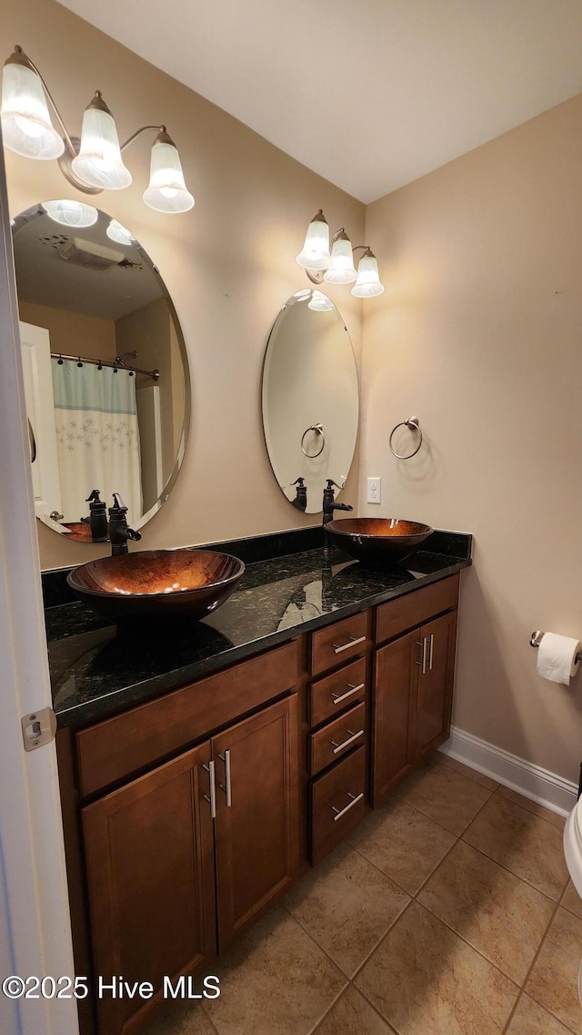 full bathroom with double vanity, tile patterned flooring, a sink, and baseboards