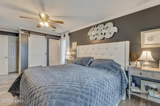 bedroom featuring a textured ceiling, ceiling fan, a barn door, and wood finished floors