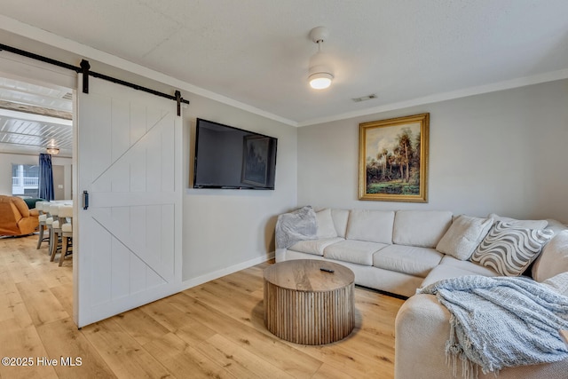 living room with a barn door, baseboards, visible vents, ornamental molding, and wood finished floors