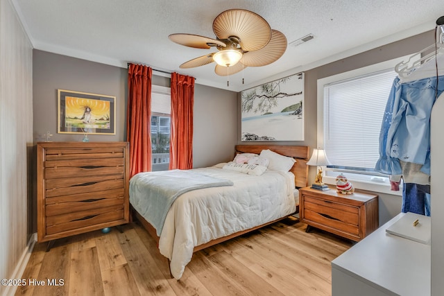 bedroom with a textured ceiling, light wood-type flooring, visible vents, and a ceiling fan