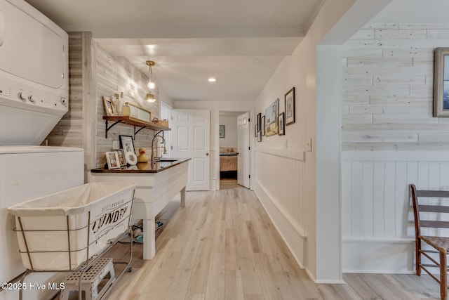 corridor with stacked washer / dryer, a wainscoted wall, a sink, and light wood finished floors