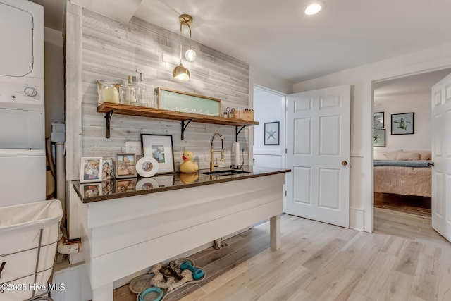 bar featuring stacked washing maching and dryer, light wood-style flooring, and a sink