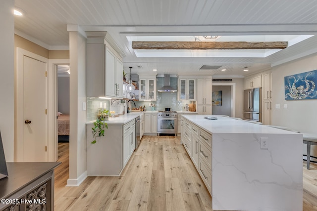 kitchen with a center island, stainless steel appliances, glass insert cabinets, white cabinets, and wall chimney range hood