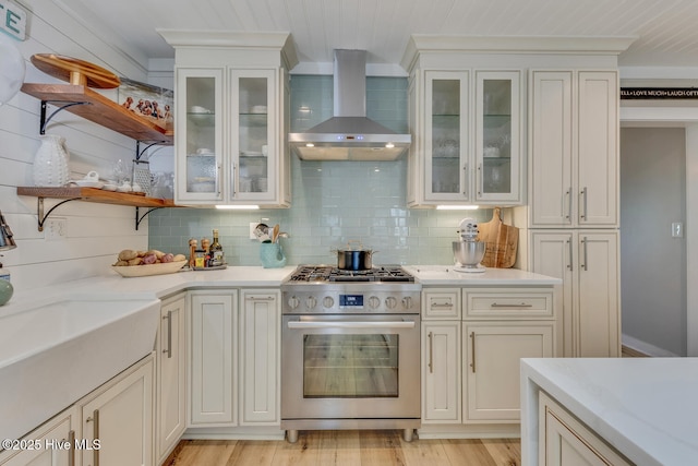 kitchen featuring wall chimney exhaust hood, glass insert cabinets, open shelves, and gas range