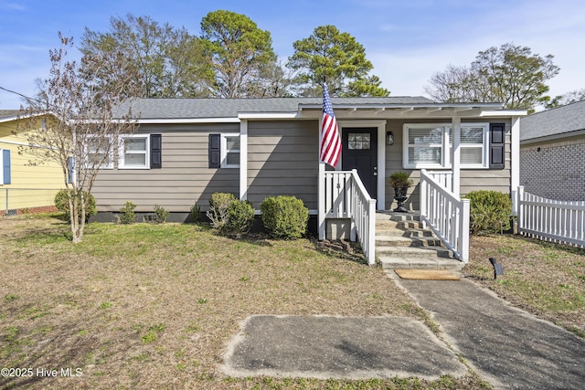 view of front facade featuring a shingled roof, a front yard, and fence