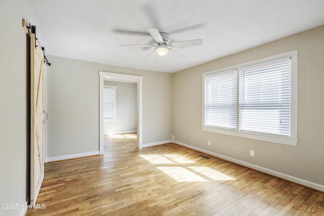 unfurnished room with a barn door, light wood-style flooring, visible vents, baseboards, and a ceiling fan