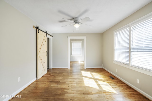 spare room featuring a barn door, visible vents, baseboards, a ceiling fan, and wood finished floors