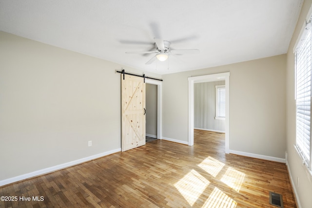 unfurnished room with a barn door, a ceiling fan, baseboards, visible vents, and light wood-style floors