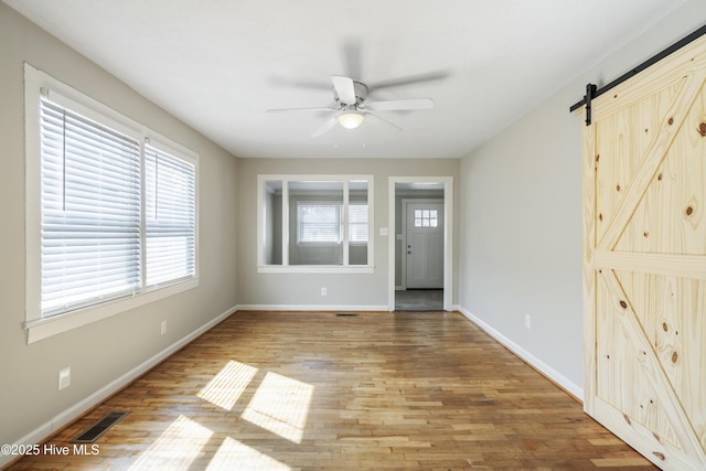 foyer featuring visible vents, a barn door, a ceiling fan, wood finished floors, and baseboards