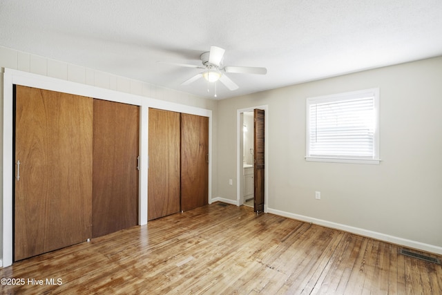 unfurnished bedroom with multiple closets, visible vents, hardwood / wood-style floors, a textured ceiling, and baseboards