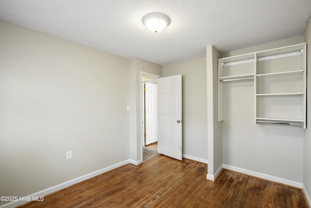 unfurnished bedroom featuring a textured ceiling, a closet, wood finished floors, and baseboards