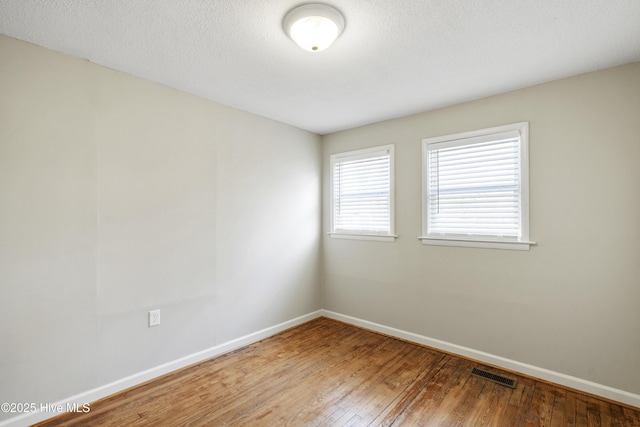 empty room with hardwood / wood-style flooring, baseboards, visible vents, and a textured ceiling