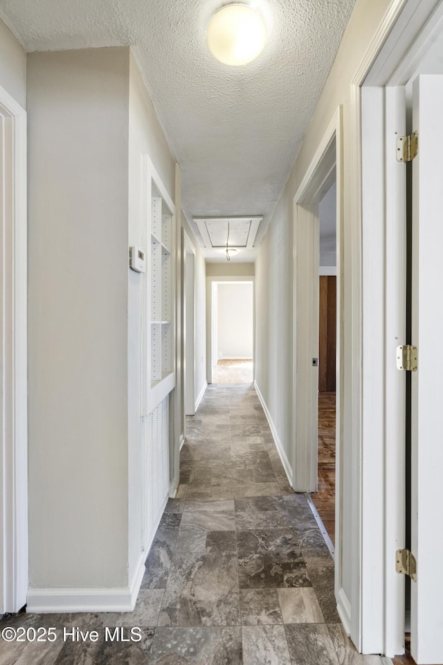 hallway with attic access, baseboards, a textured ceiling, and stone finish flooring