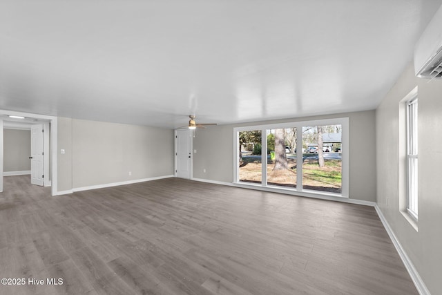 unfurnished living room featuring ceiling fan, a wall unit AC, wood finished floors, and baseboards