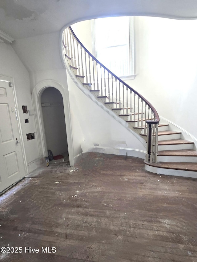 foyer featuring stairs, arched walkways, and dark wood finished floors