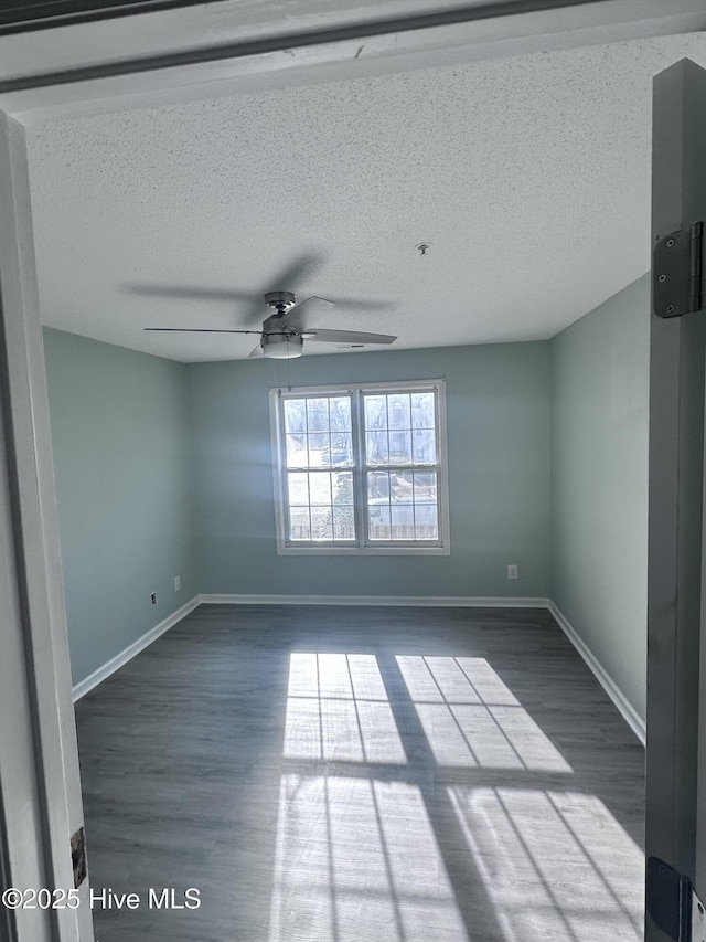 unfurnished room featuring a ceiling fan, a textured ceiling, baseboards, and dark wood-type flooring