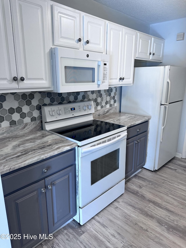 kitchen with light wood finished floors, white appliances, white cabinetry, and tasteful backsplash