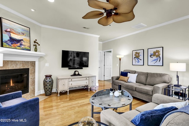 living room featuring light wood finished floors, a fireplace, visible vents, and crown molding