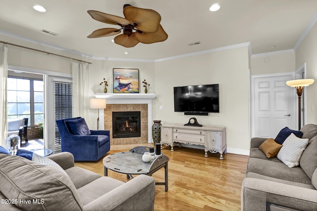 living area featuring ornamental molding, light wood-style flooring, a tile fireplace, and visible vents