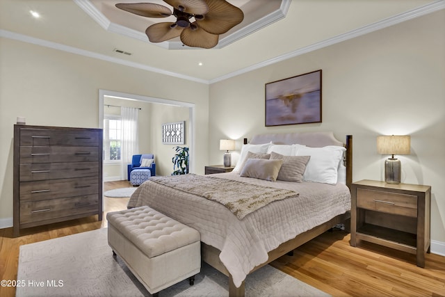 bedroom with a raised ceiling, visible vents, crown molding, and wood finished floors