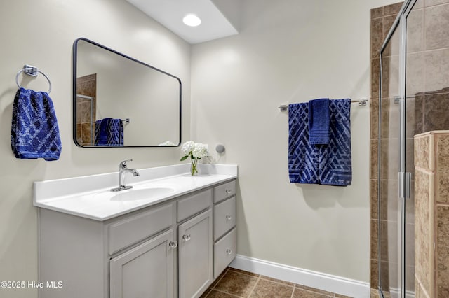 bathroom with a tile shower, vanity, and baseboards