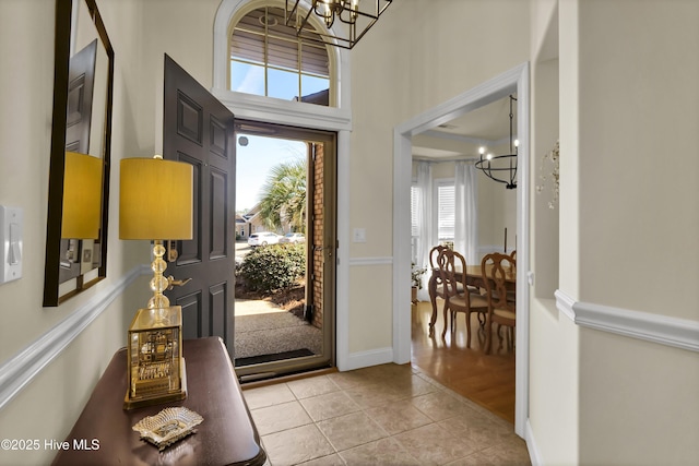 foyer entrance featuring baseboards, a chandelier, and light tile patterned flooring