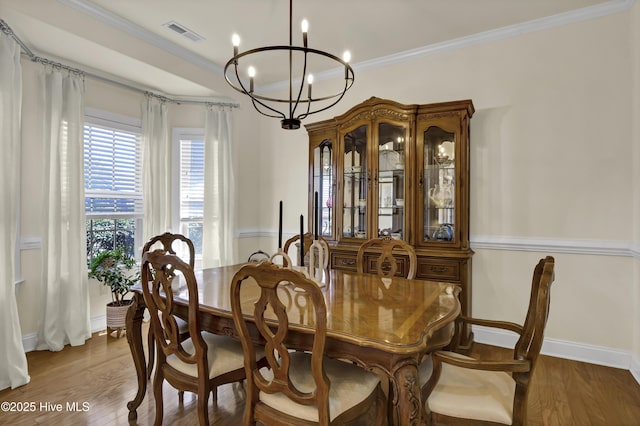 dining space with visible vents, ornamental molding, a notable chandelier, and wood finished floors