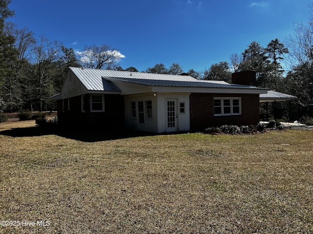 view of front of property featuring brick siding, metal roof, a chimney, and a front lawn