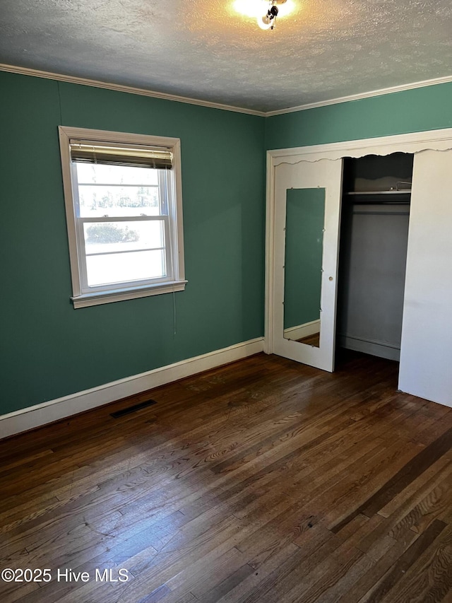 unfurnished bedroom featuring dark wood-style flooring, a closet, visible vents, and crown molding