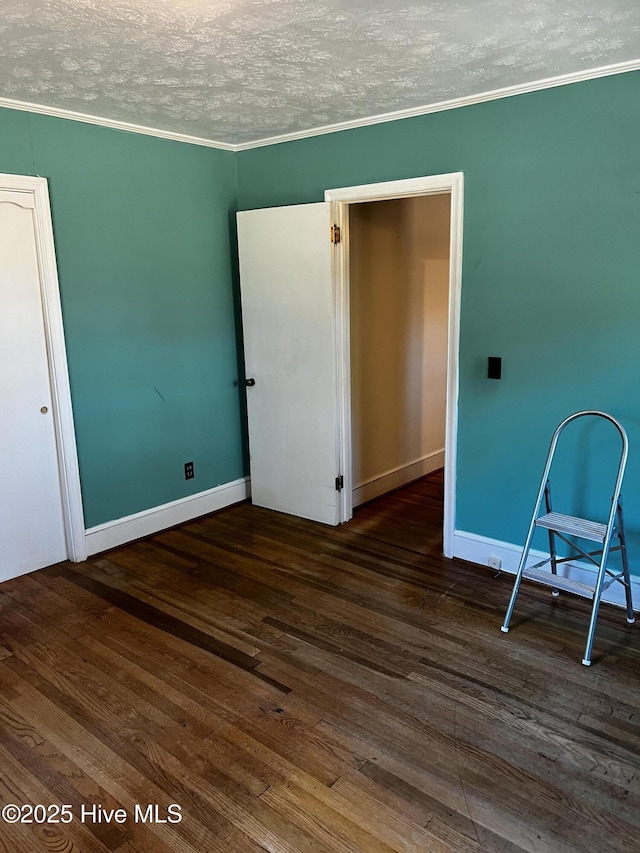 empty room featuring dark wood-style floors, ornamental molding, a textured ceiling, and baseboards