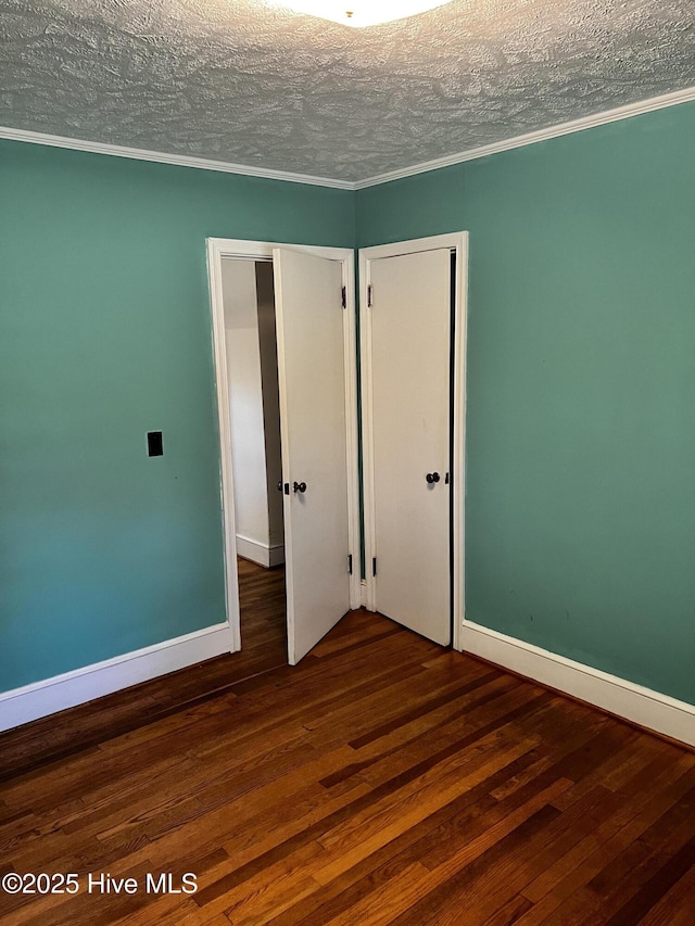 spare room with a textured ceiling, baseboards, dark wood finished floors, and crown molding