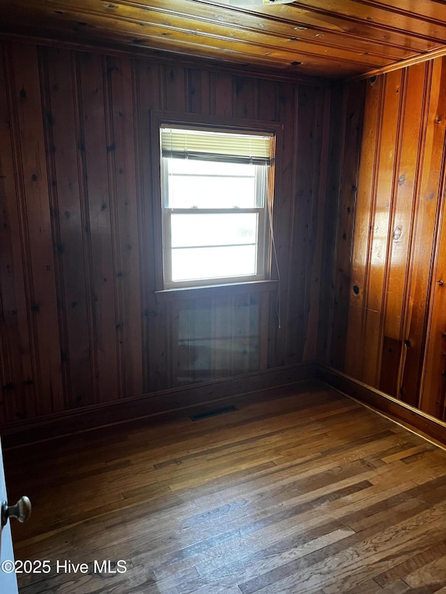 empty room featuring wooden walls, visible vents, and dark wood finished floors