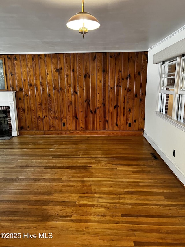 unfurnished dining area featuring wooden walls, visible vents, baseboards, a brick fireplace, and dark wood-style floors