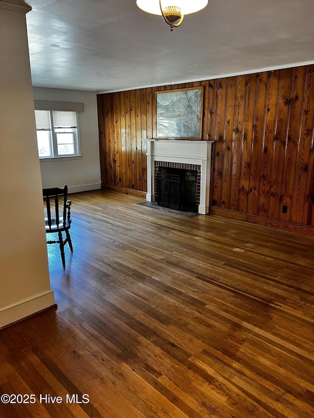 unfurnished living room with wooden walls, a fireplace, baseboards, and dark wood finished floors