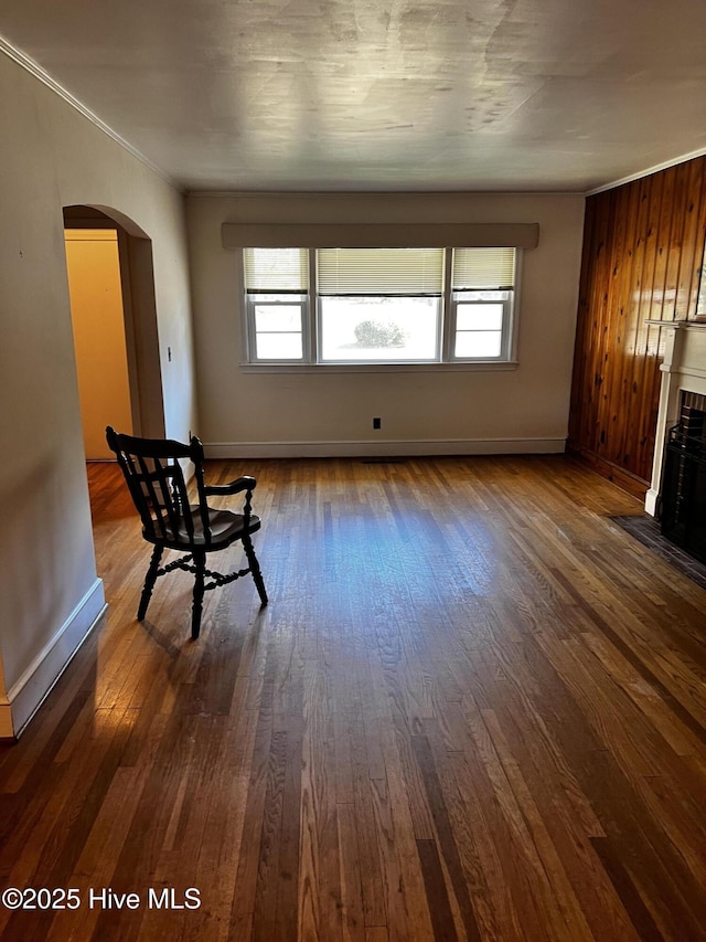 unfurnished room with arched walkways, dark wood-style flooring, a fireplace with flush hearth, and baseboards