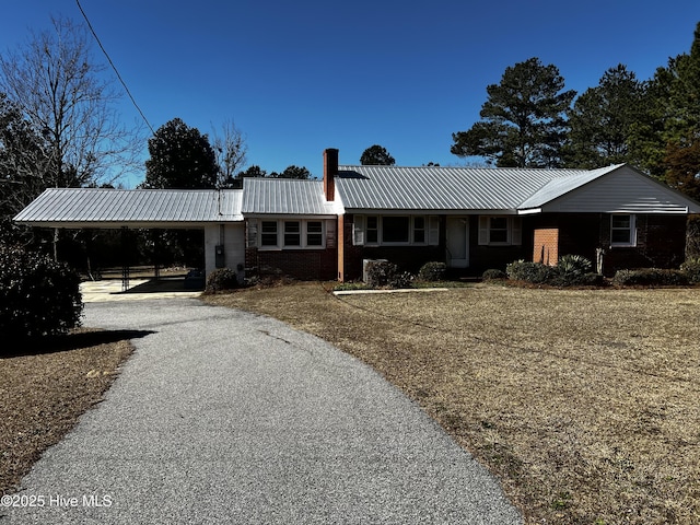 view of front of property with driveway, a chimney, metal roof, an attached carport, and brick siding