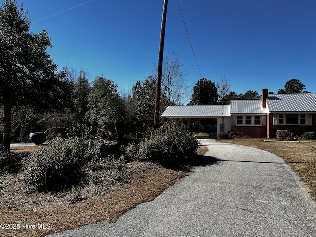 view of front of home featuring a chimney, metal roof, and driveway