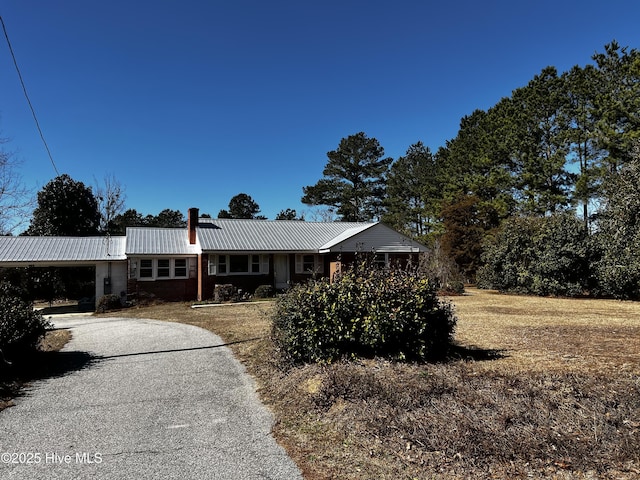 ranch-style home with driveway, brick siding, metal roof, and a chimney