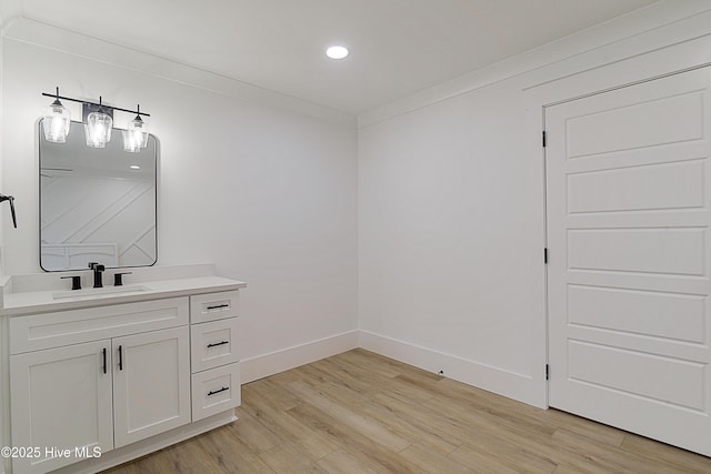 bathroom with recessed lighting, ornamental molding, vanity, wood finished floors, and baseboards